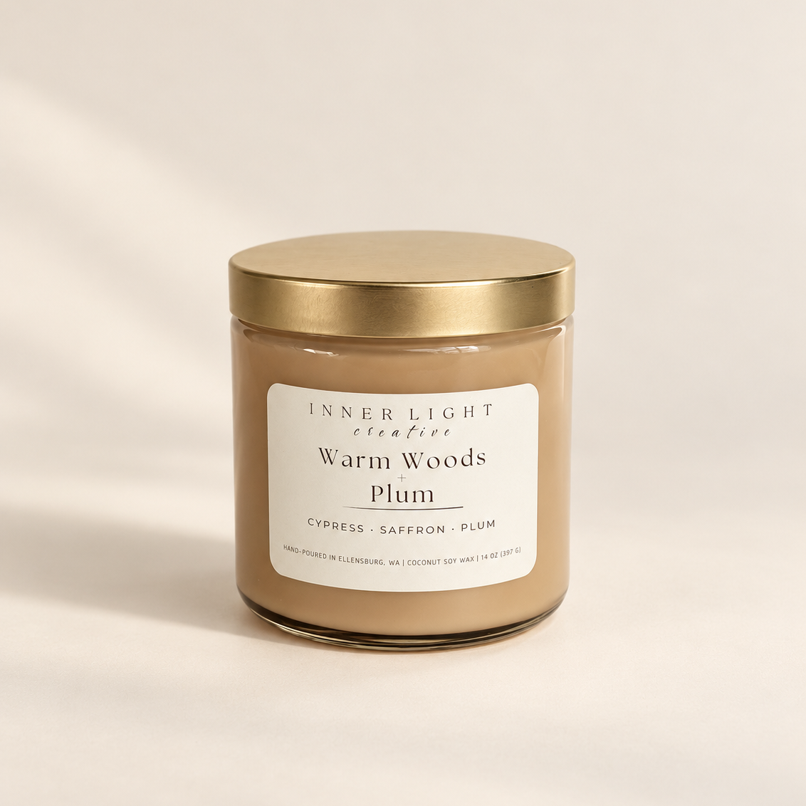Inner Light Creative Warm Woods + Plum coconut soy candle in an oatmeal-colored glass jar with a gold lid and cream label.