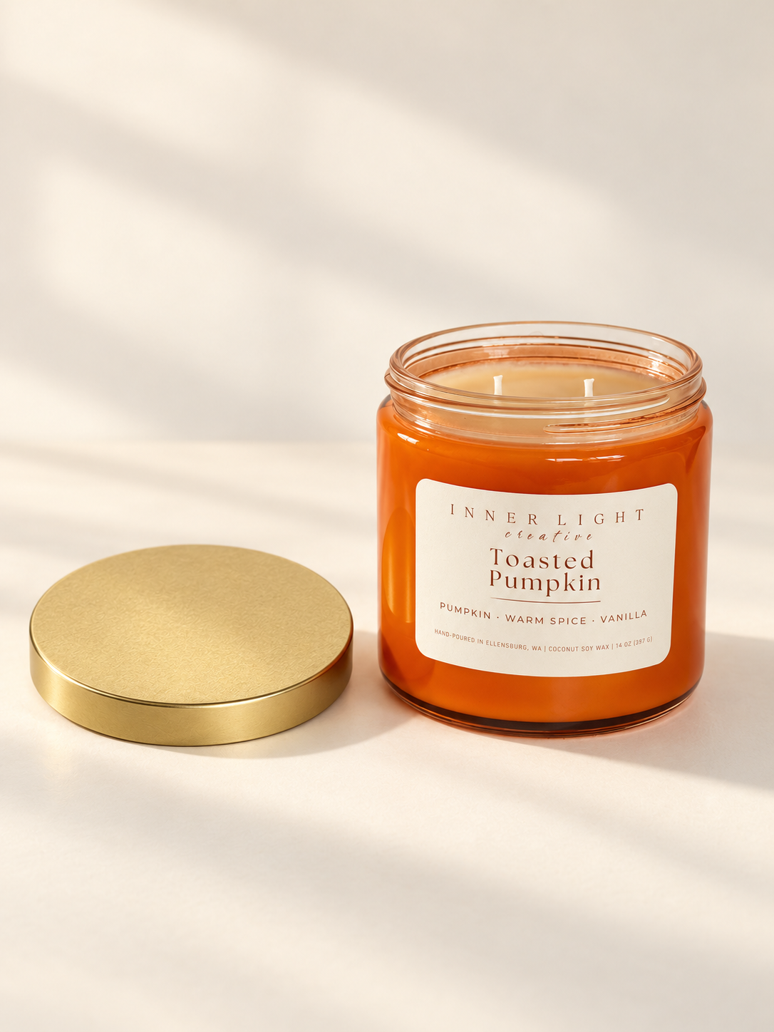 Inner Light Creative Toasted Pumpkin candle in an orange glass jar, showing two cotton wicks with the gold lid beside it.