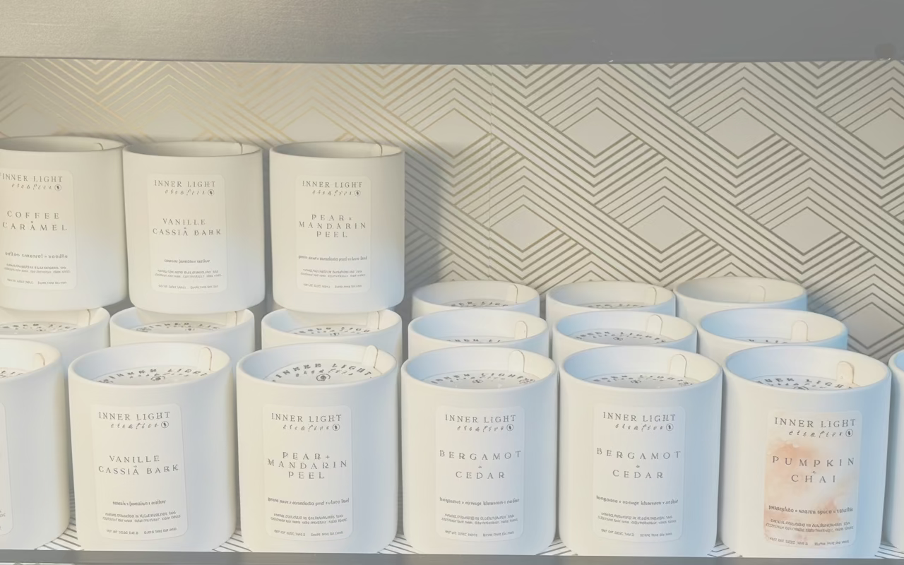 Row of candles with labels on a shelf against a geometric-patterned wall.